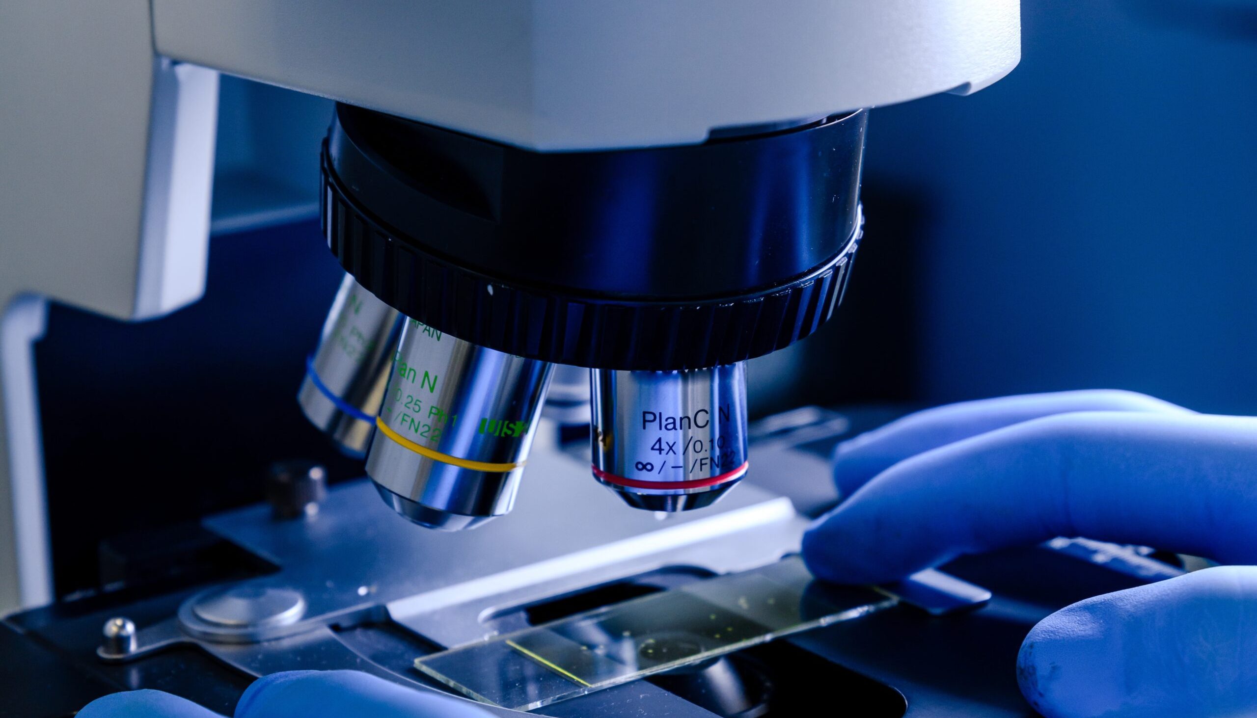 A vertical closeup shot of a laboratory worker working with a modern microscope while conducting a coronavirus research